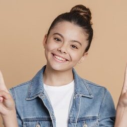 Positive, smiling teenage girl showing V gesture. The girl joyfully gestures on a brown background
